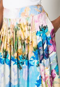 Saia com estampa floral e pregas; apresenta tons de azul, rosa e verde em tecido suave; a cintura contém um design floral discreto.