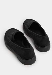Scarpe slip-on in suede nero con una forma arrotondata, dotate di un profilo basso e cuciture visibili lungo i bordi.