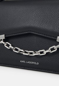Borsa a mano nera in pelle con finitura testurizzata, hardware in catena argentata e logo del marchio in rilievo sul fondo.