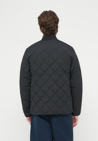 Czarna pikowana kurtka z wysokim kołnierzem, wzorem diamentowym oraz elastycznymi mankietami, zaprojektowana z myślą o ciepłu i wygodzie.