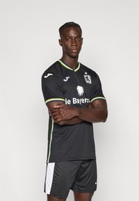 Juodas futbolo marškinėlis su trumpomis rankovėmis, mėlynos ir geltonos spalvų apvadais, liūto emblemą ir užrašu „Die Bayern“. Derinamas su juodomis trumpikėmis.