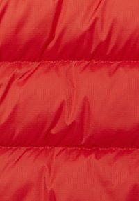 Rood gevoerd stof met een gladde textuur en horizontale gestikte secties. Het materiaal lijkt lichtgewicht en waterafstotend.