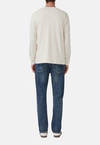 Cream long-sleeve t-shirt with a round neckline paired with blue denim jeans. The jeans have a classic five-pocket design and a faded texture.