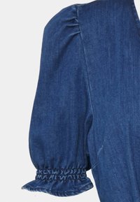 Blusa de ganga azul com mangas curtas bufantes e punhos elásticos, apresentando uma textura suave e um decote limpo.