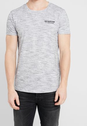Mann trägt ein graues meliertes kurzärmeliges T-Shirt mit dem "Tom Tailor Denim"-Logo auf der oberen linken Brust und schwarze Jeans.