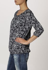 Blusa de flores azul marino con mangas tres cuartos, escote fruncido y un corte holgado. La tela presenta patrones florales blancos sobre un fondo oscuro.