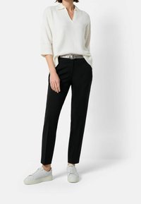 Kremowy sweter z dekoltem w serek i krótkimi rękawami, zestawiony z czarnymi, dopasowanymi spodniami i białymi trampkami. Posiada srebrny pasek.