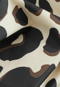 Stof met een beige basis voorzien van grote, onregelmatige zwarte en bruine leopardvlekken, met een getextureerde, geweven uitstraling.