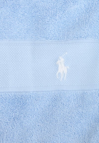 Ανοιχτό μπλε πετσέτα με υφασμάτινη υφή και λευκό κεντημένο λογότυπο με άλογο και αναβάτη που κρατά ρακέτα πόλο σε υφασμένη ταινία.