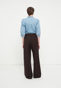 Lyseblå denimskjorte med pufferm, samlet mansjett, kombinert med høytlivede, vide brune bukser. Rent, enkelt design.