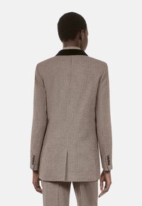 Hnědý blazer s houndstooth vzorem, černým sametovým límcem, úzkým střihem a tailored rukávy, se zapínáním na knoflíky na manžetách.