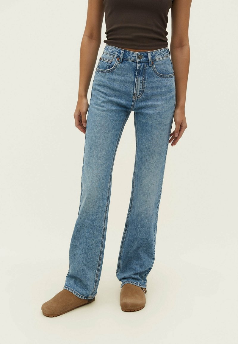 Jean évasé bleu clair en denim. Comprend cinq poches, une fermeture par bouton et zip, et une taille haute.