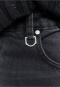 Black denim fabric with a visible pocket, accented by a silver metal button and a contrasting flat black drawstring. Textured knit above.