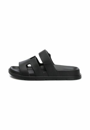 Sandalia tipo slide de cuero negro con dos tiras anchas, recortes y suela texturizada. Presenta un diseño plano y una construcción resistente.