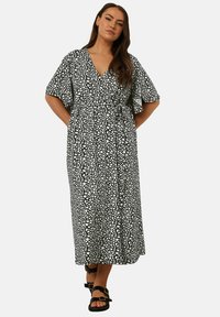 Svart och vit mönstrad omslagsklänning med korta volangärmar, midjeband och en flödande kjol, tillverkad av lättviktig tyg.