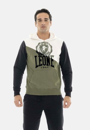 Uomo che indossa una felpa con cappuccio a blocchi di colore con sezioni bianche, verde oliva e nere e il logo "LEONE 1947", in piedi con le braccia rilassate.