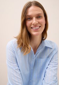 Camicia azzurra chiara con strisce bianche verticali, maniche lunghe e taschino sul petto, caratterizzata da una texture di tessuto morbida.