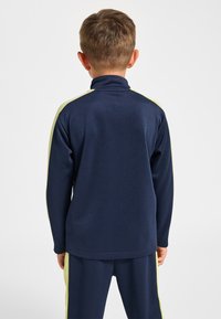 Marinblå sporttopp med hög krage och ljusgröna sidostripes. Slät textur, åtsittande passform och ribbade muddar. Designad för aktivt bruk.