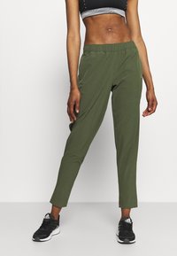Green athletic pants made of lightweight fabric, featuring an elastic waistband, tapered design, and front pockets. Paired with black sneakers.