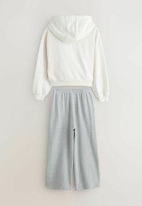 Witte hoodie met manchetten, gecombineerd met grijze wide-leg sweatpants met een elastische tailleband. Gladde texturen overal.