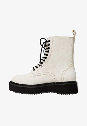 Botín blanco con cordones hasta el tobillo, con una superficie texturizada, suela de plataforma negra y cordones en contraste. Presenta un diseño minimalista con líneas limpias.