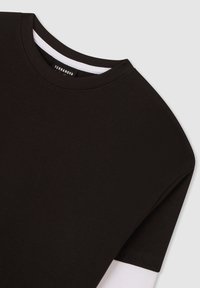 Czarny bawełniany t-shirt z okrągłym dekoltem, krótkimi rękawami i warstwowym designem, z białą warstwą widoczną na krawędzi.