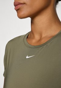 Camiseta Nike verde oliva con cuello redondo y mangas cortas, que presenta un pequeño logo swoosh blanco en la parte frontal. Textura suave.