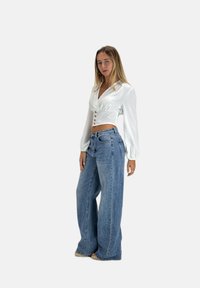 White long-sleeve crop top with a deep V-neck and front button closure, paired with light blue high-waisted wide-leg jeans.