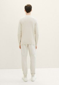 Suéter beige claro con un patrón texturizado, combinado con pantalones grises claros ajustados y zapatillas blancas. Vista desde la parte posterior.
