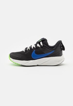 Black athletic shoe with a textured upper, blue swoosh, white laces, and a green rubber outsole. Features a cushioned midsole and heel tab.