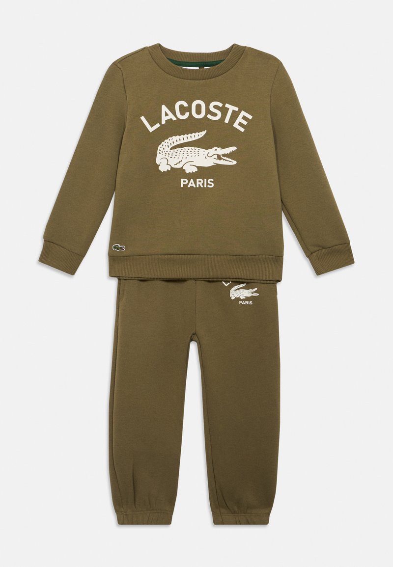 Conjunto de sweatshirt de mangas longas e calças na cor verde oliva, com o logo branco da Lacoste e um gráfico de crocodilo no peito e na perna esquerda das calças.