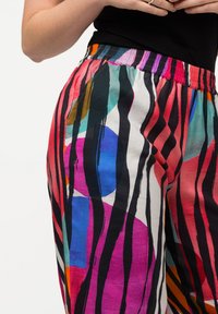 Pantaloni colorati caratterizzati da un mix di forme astratte in rosso, blu, verde e viola, con strisce verticali nere a contrasto e una cintura elastica.