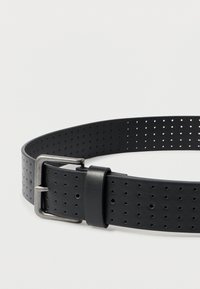 Fekete bőrből készült öv, egyenletesen elhelyezett kör alakú perforációkkal és ezüstszínű, téglalap alakú csattal világos háttéren.