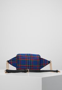 Rutig handväska med blå, gröna och röda mönster, med yttertyg av tyg och detaljer i guldton. Inkluderar en svart justerbar rem.