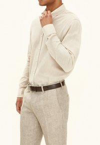 Lichtbeige longsleeve shirt met een button-down kraag, gemaakt van gemercerwe stof, gedragen met lichtgekleurde broeken en een bruine leren riem.