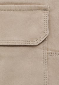 Nahaufnahme eines beigen Stoffes mit einer genähten Klappentasche, die doppelt genähte Nähte und ein gerades Kanten-Design aufweist.