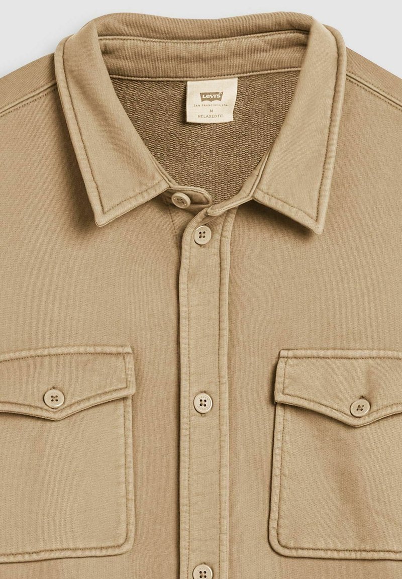 Beige overhemd met knopen, gemaakt van een zachte, gestructureerde stof met een kraag, twee borstzakken en vier knopen aan de voorkant.