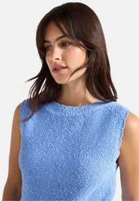 Blauwe mouwloze top met een ronde, ribbelige halslijn. Gelaagd breiwerk met een subtiel patroon. Randen zijn afgewerkt met een geschulpt design.