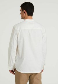 Camicia bianca a maniche lunghe con vestibilità relaxed, caratterizzata da una trama testurizzata, polsini con bottoni e un piccolo etichetta sul lato sinistro vicino all'orlo.