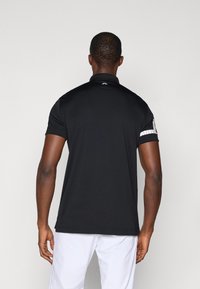 Camisa polo preta com mangas curtas, colarinho plano e detalhes listrados em branco nas mangas. Tecido suave com um design ajustado.