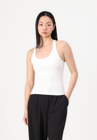 Witte mouwloze tanktop gemaakt van glad, rekbaar materiaal, met een ronde halslijn en een getailleerd silhouet, gecombineerd met zwarte broek.