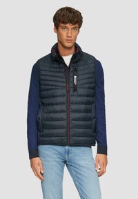 Marineblauer Stepp-West mit gesteppter Textur, Reißverschluss vorne und Stehkragen. Verfügt über blaue Strickärmel und dezente rote Akzente am Reißverschluss.