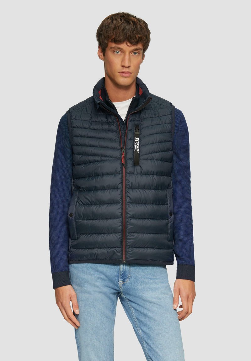 Marineblauer Stepp-West mit gesteppter Textur, Reißverschluss vorne und Stehkragen. Verfügt über blaue Strickärmel und dezente rote Akzente am Reißverschluss.