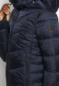 Prošívaná bunda v námořnické modři s opakujícím se vzorem "FIRE". Má zipové zapínání, boční kapsu a texturovaný povrch.