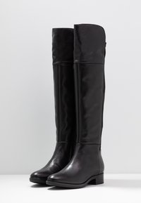 Botas altas de cuero negro con un acabado suave, punta redonda y tacón bajo en bloque; cuentan con una cremallera lateral y un diseño de puño doblado.
