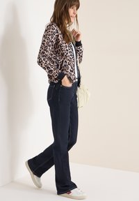 Bomberjack met luipaardprint en zwarte boorden, gecombineerd met donkerblauwe jeans en witte sneakers. Casual outfit met een ontspannen pasvorm.