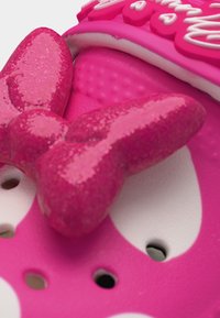 Gros plan sur une sandale rose avec des accents blancs, ornée d'une décoration papillon rose brillante et de petits trous de ventilation.