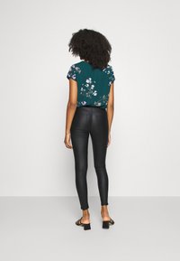 Camisa verde con estampado floral y mangas cortas, combinada con leggings negros ajustados. El conjunto presenta una textura suave y un hardware minimalista.
