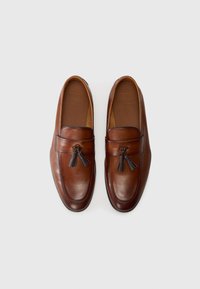 Mocasines de cuero marrón para hombre con flecos, punteras redondeadas y plantillas grabadas, dispuestos uno al lado del otro sobre un fondo blanco.