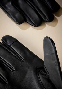 Sorte læderhandsker med en glat tekstur, der har syet detaljer og et tapered design. Fingerspidserne viser subtile kontrasterende accenter.
